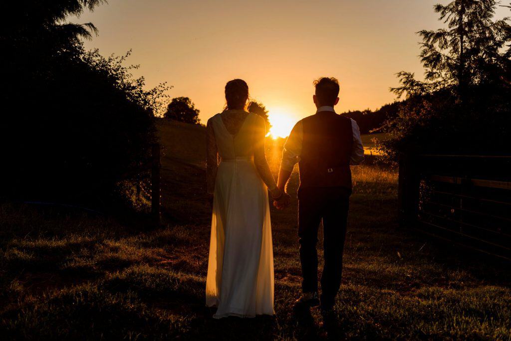 Bridal couple standing hand in hand silhouetted in sunset