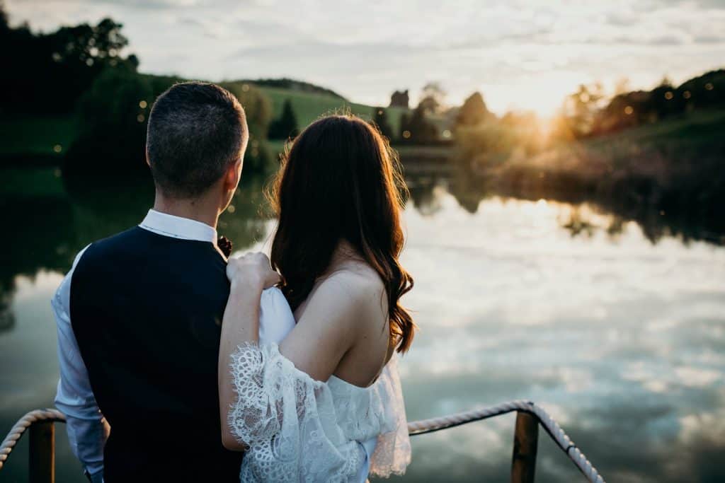 Bridal couple looking out over a sunset lake