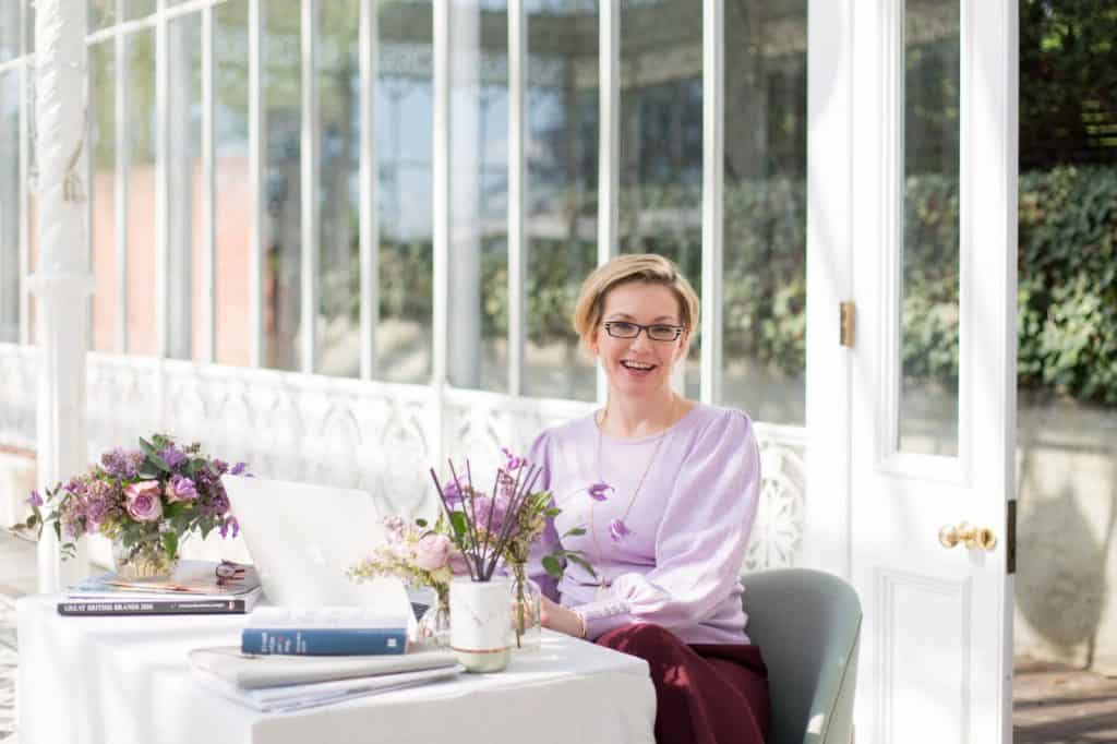 Lady wearing lavender sitting at a table working on an apple mac