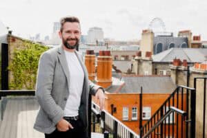 Kelly Chandler on a rooftop terrace with city skyline in background.