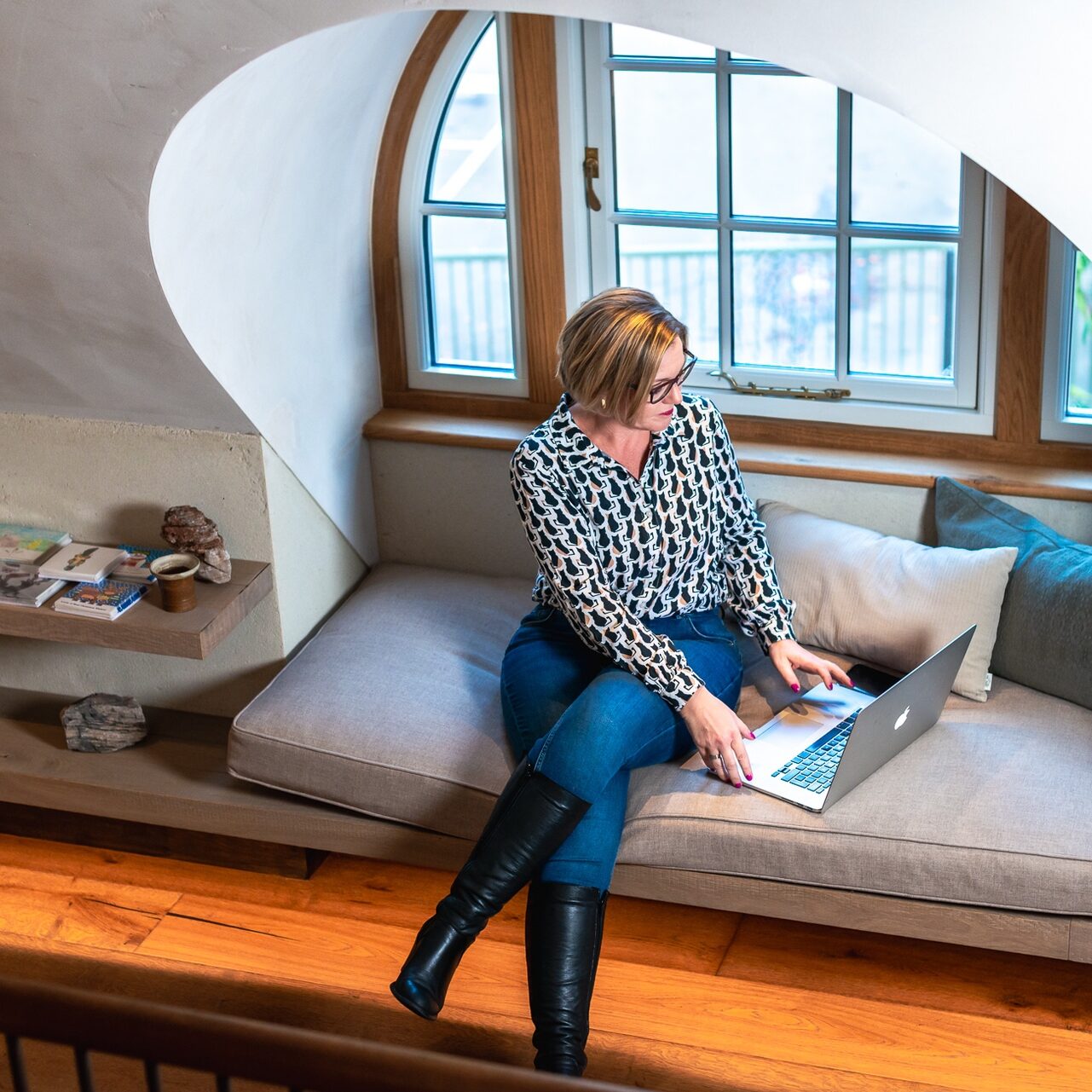Woman working on a laptop in a cosy attic space with large window.